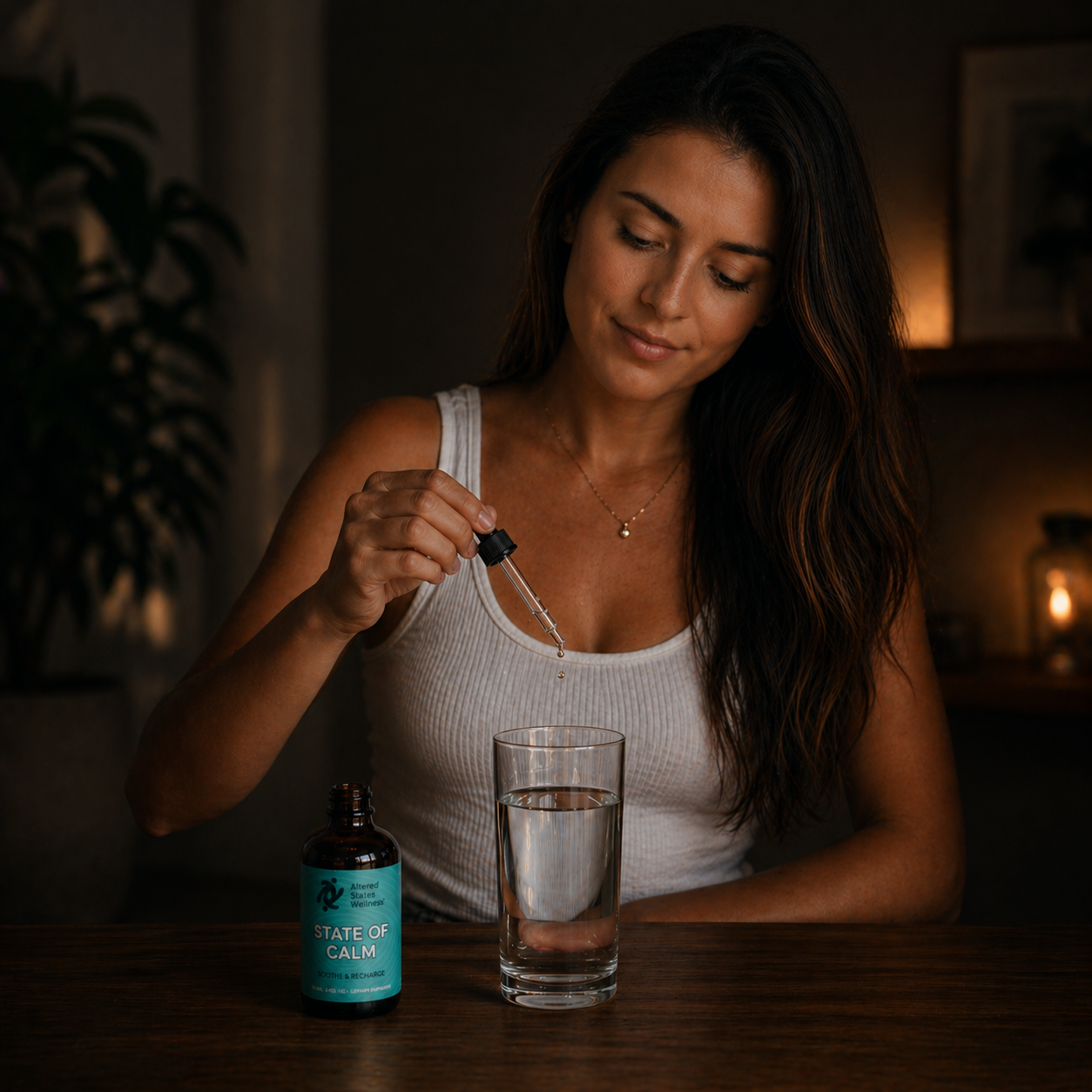 Woman pouring a liquid from a dropper into a glass of water with a bottle labeled 'State of Calm' on a wooden table.